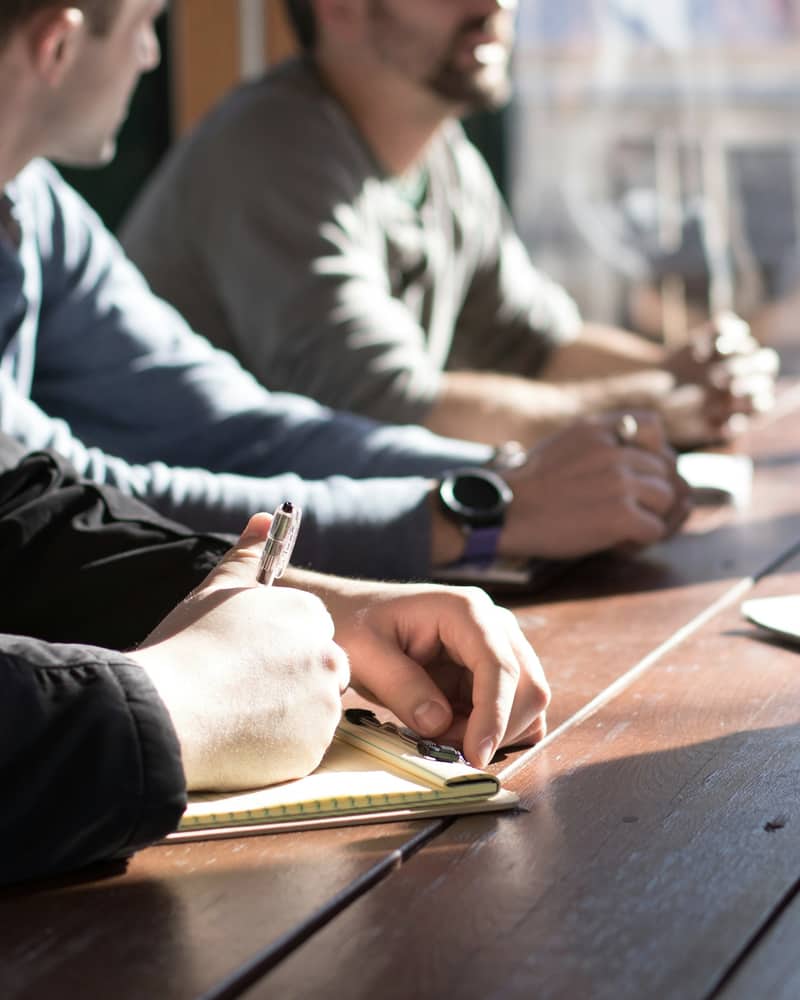 Hands taking notes at a sunlit meeting table